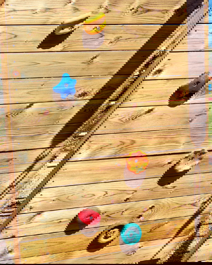 Holzkletterwand mit farbenfrohen Halten, einschließlich gelb, blau, orange, rot und türkisfarben, unter Sonnenlicht. Schlüsselattraktion für Outdoor -Aktivitäten.