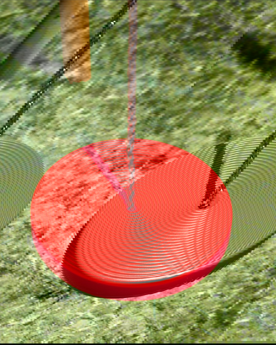Rotkreisscheibenschwung mit strukturierter Oberfläche, die in einem Spielplatz von einem Seil über grünem Gras hängt. Perfekt für Spaß im Freien und die Aktivitäten von Kindern.